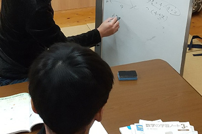 ホワイトボードに書き込む講師の手と、生徒の後頭部の写真