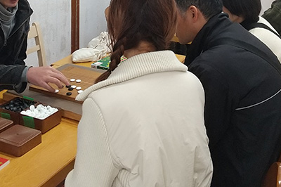 囲碁指導する手と、囲碁指導を受ける３人の親子